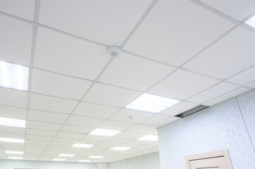 clean office space with Armstrong ceiling tiles, recessed LED lights, white textured walls, a wooden door, and a smoke detector mounted on the ceiling.