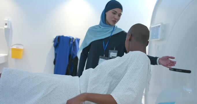 Radiology tech gesturing, guiding African American patient on scanner table, aligning head for CT