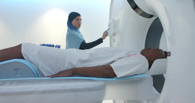 Male patient and tech in hijab preparing CT scan in CT suite, adjusting panel, confirming alignment