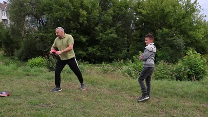 A man throws a training pad to a boy, working on reaction and coordination during an active outdoor practice.