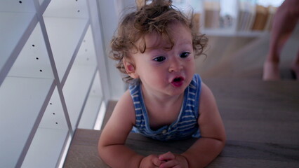 Fototapeta premium Toddler pauses on stairs and looks up with expressive face, captured mid-sound or question in bright modern home filled with books and natural textures