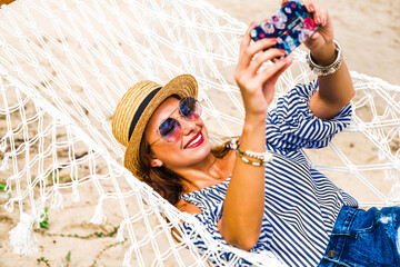 Happy beautiful girl in a straw hat and shorts, striped t-shirt, lying on a beach hammock between...
