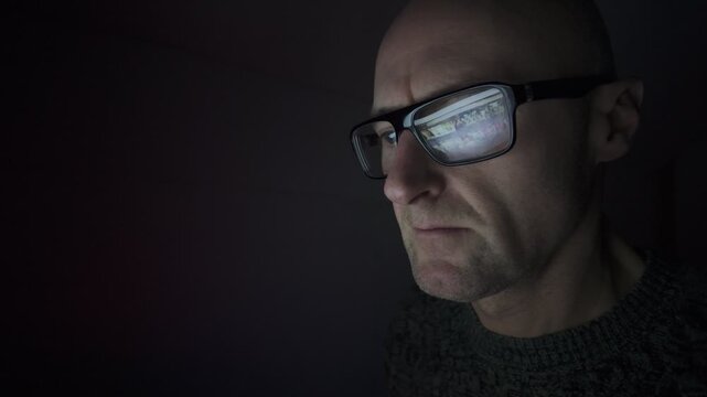 CU Man sat in dark room using a computer, refection in his glasses. Hacker, on-line dating, social media.