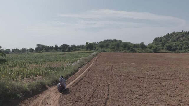 Indian farmer couple riding motorbike in rural farmland