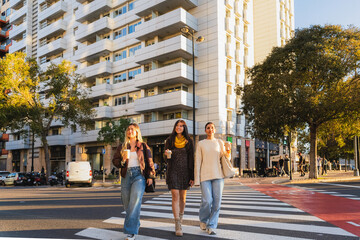 Three friends enjoying afternoon walking on a pedestrian crossing with coffee cups