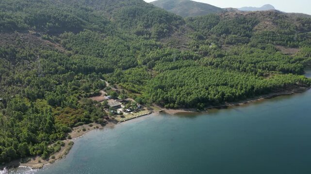Aerial drone view of a small campsite and RV parking area on the forested shores of Lake Komani, Albania, featuring turquoise water and rugged mountain peaks in the Balkan wilderness.