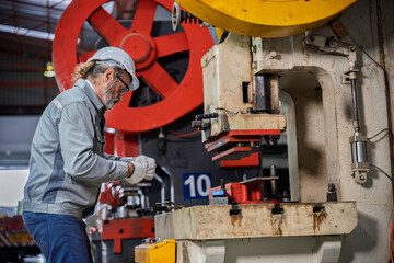 Senior industrial worker operating a heavy hydraulic press machine within a large metal manufacturing plant. Experienced engineer controlling the production process.