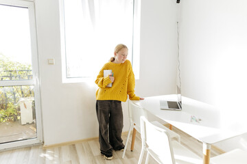 Teenage girl standing by desk with laptop and notebook, student preparing for online learning at home, distance education concept, focused study routine