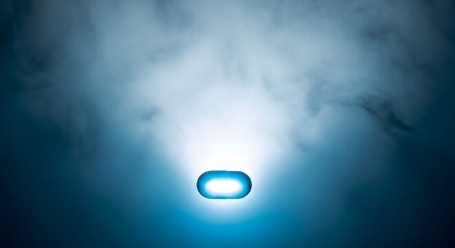 Glowing blue capsule pill floating in a dramatic, dark, smoky en
