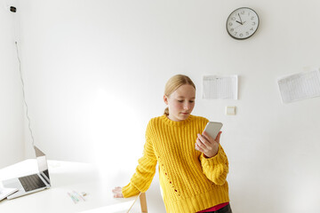 Teenage girl checking smartphone during home study, student distracted from learning, modern education at home, time management problem, digital habits