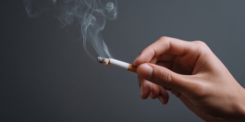 Hand holding burning cigarette against smoky gray background