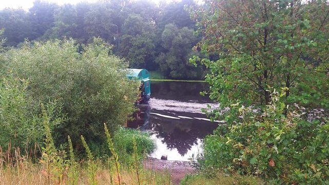 A boat rests on the calm surface of the river. Surrounding trees and plants create a natural setting. This spot is ideal for relaxing and enjoying the outdoors.