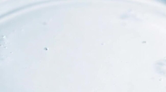 Close up view of a pure water drop falling onto a clear liquid surface creating circular concentric ripples and a splash crown, water video.
