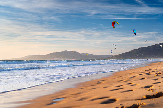 Kites fly against the sky at sunset on coast with mountains in the background at famous surfing spot in Europe, Spain, Tarifa.