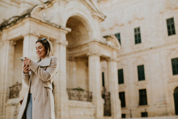 Woman walking and using phone in Malta during the day near historic buildings