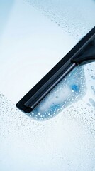 A black squeegee wipes a wet glass surface, leaving clear streaks. The image conveys cleanliness, freshness, and efficiency. Useful for cleaning product ads or service promotions.