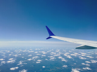 View from airplane window to airplane wing, and clouds from above the sky.