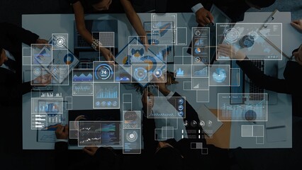 A high-angle view showcasing a group of professionals collaborating over data analysis with various digital graphs and charts displayed on screens in a modern office. Raster