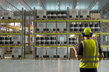 Warehouse, industrial storage facility. Safety supervisor monitors chemical containers and pallets...