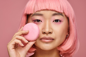 Young woman with pink hair holds a pink macaron against a soft pink background