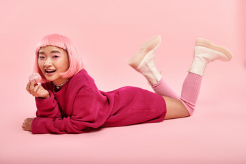 Young woman enjoys sweet treat in playful pink outfit against a vibrant background