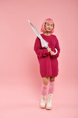 Stylish young woman holding a transparent umbrella against a soft pink backdrop