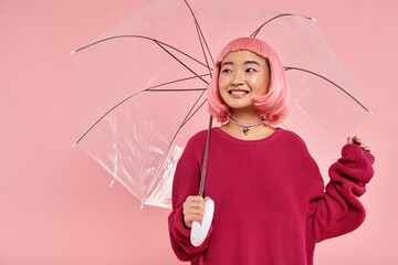 Joyful young woman embracing happiness under a transparent umbrella in a vibrant pink setting