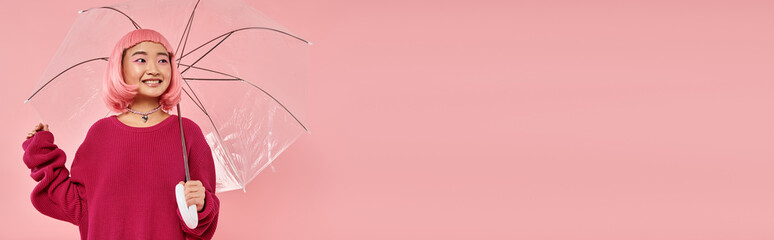 Young woman in pink sweater joyfully poses with a clear umbrella against a soft pink backdrop