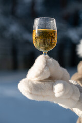 Hand in white fur mitten holding champagne glass outdoors in winter, luxury detail