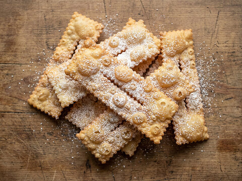 Top view of traditional Italian carnival fried pastries dusted with powdered sugar on rustic wooden table.