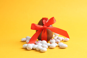 Happy Easter. Chocolate egg with bow and candies on yellow background, closeup