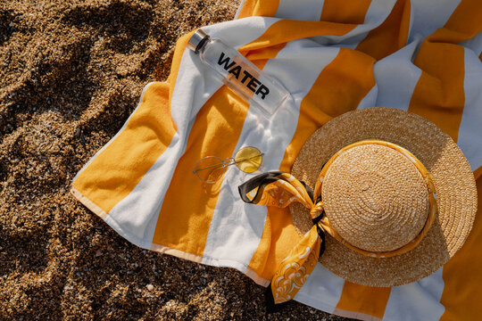 flat lay view from above on summer vacation beach items, yellow beach towel on sand, straw hat, sunglasses, water bottle, trip to Italy