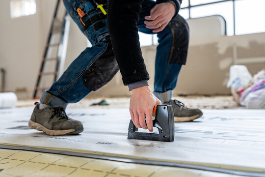 Artisan en train de fixer des panneaux isolants au sol avec une agrafeuse lors de travaux de r&eacute;novation int&eacute;rieure, illustrant la pose et l&rsquo;isolation d&rsquo;un chantier moderne.