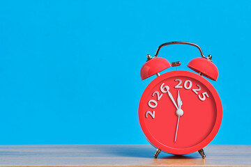 Red alarm clock on blue background shows transition from 2025 to 2026. Symbol new age. Copy Space.