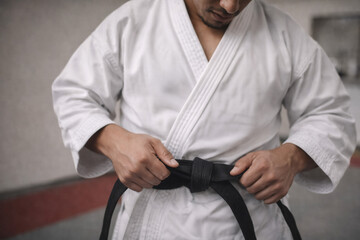 karate practitioner tying black belt in dojo