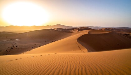 Vast dunes roll under the warm glow of a sunrise, casting shadows and revealing the textured landscape. Mountain silhouettes