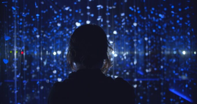 Silhouetted young adult gazing intently at a vibrant, immersive blue light art installation with countless glowing hearts, representing wonder, digital connection, and a contemplative future.