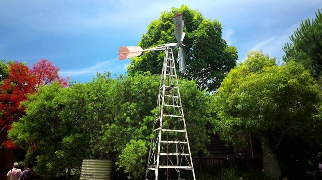 Old Farm Windmill Spinning Above Lush Garden Trees