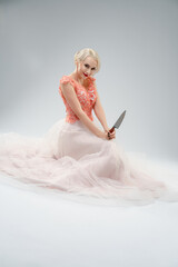 Bride in a blood-splattered gown holds a knife while posing in a studio