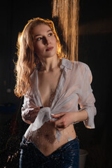 Woman with wet shirt poses under water stream in dimly lit environment