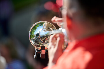 Close-up of trumpet reflection capturing outdoor scene with musician in red