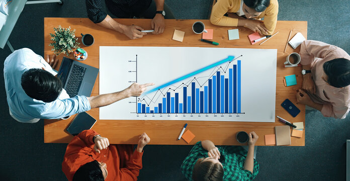 A diverse team gathered around a table engaged in a productive meeting, analyzing a data chart to strategize and enhance business growth and performance. Scalp - Powered by Adobe
