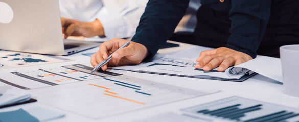 Business professionals engage in collaborative data analysis with reports and charts on a desk, using a laptop in a modern office, enhancing teamwork and productivity. SACTR