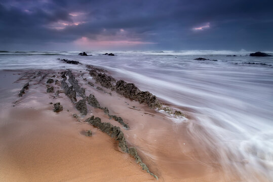Long exposure of flysch rock formations on Atxibiribil beach under a stormy sky, Sopelana, Spain