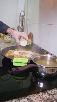 Person adding rice to a paella pan for traditional Spanish cuisine