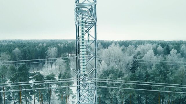 Orbiting aerial view of frozen suspension insulators and power cables on a transmission tower, revealing icy details and snow covered forest during a cold winter day.