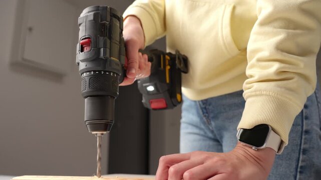 Close up of person using cordless power drill with drill bit to drill hole in wooden board. Concept of DIY, woodworking