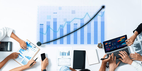 A modern business team collaborates in an office setting, analyzing financial data using laptops and charts to strategize for growth and performance improvements. Axiom