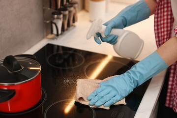 Woman spraying cleaning product while wiping dust from cooktop in kitchen, closeup