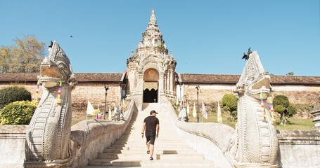 Obraz premium Young Asian man confidently ascending ornate naga-flanked steps towards a majestic Buddhist temple, embodying exploration, spirituality, and cultural discovery in Southeast Asia.